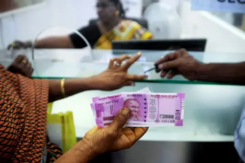Getty Images In this photograph taken on November 17, 2016, an Indian woman holds 2000 INR notes as she has her finger marked with indelible ink after exchanging 500 and 1000 INR banknotes at a bank in Chennai. India's government acknowledged January 31 that its decision to pull high-value bank notes from circulation has caused pain in large parts of the economy as it lowered its growth forecast on the eve of the budge