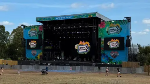 BBC An empty stage at Kendal Calling, with the festival branding. There are a handful of people in the field in front of the stage milling around.