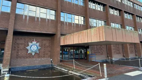Ben Parker/BBC The outside of a police building. It is built with brown bricks and for-storeys high. There is a large Suffolk Constabulary emblem attached to the outside wall. The front door is glass-panelled and under a stone covering. 
