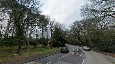 The junction of Old Woking Road and Pyrford Common Road, with a few cars driving on it.