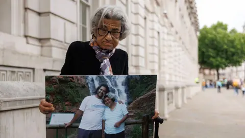 Getty Images Laila Soueif holds up a photo showing her with her son Alaa Abdel Fattah, after resuming her hunger strike outside Downing Street, London, on 28 May 2025