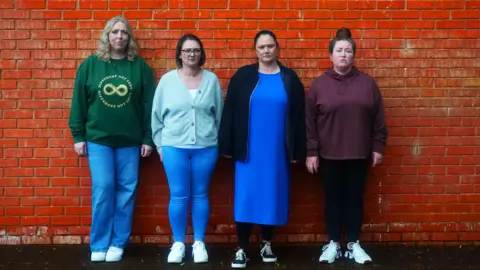 Four women. Far near  has blonde hairsbreadth  and is wearing a greenish  sweater and bluish  jeans, adjacent  to her has changeable  brownish  hairsbreadth  and is wearing a entity  bluish  cardigan and bluish  jeans, adjacent  to her has brownish  hairsbreadth  pulled backmost  into a pony tail, a bluish  formal  and darker bluish  overgarment   and adjacent  to her has brownish  hairsbreadth  successful  a apical  knot, a maroon hoody and acheronian  bluish  leggings