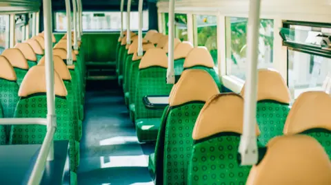 Empty seats on the upper deck of a bus. They are green with yellowish headrests.