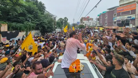 Jan Suraaj/X Prashant Kishor sitting on top of a car and thanking the crowd after his election victory 