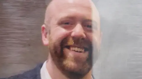 A bald man with a short brown beard smiles at the camera