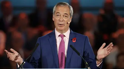 Getty Images Nigel Farage wears a navy suit and a red tie. He has grey hair and has his arms out and palms open.