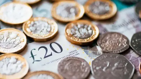 Getty Images A £20 note with gold and silver coins on top of it.