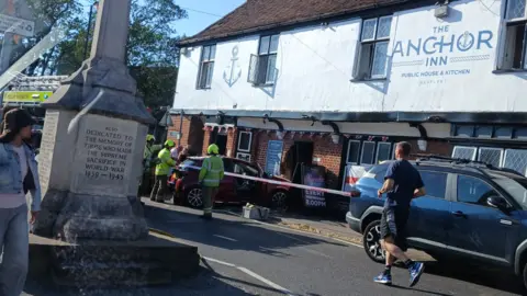 Lilly-Mae Langley The front of the pub can be seen with a vehicle having crashed into its frontage. Firefighters in yellow high-vis jackets are outside.