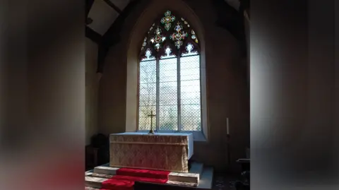 Richard Chatham A view of a church window inside St Mary's Church. The large altar sits in front of the window with steps leading up to it.