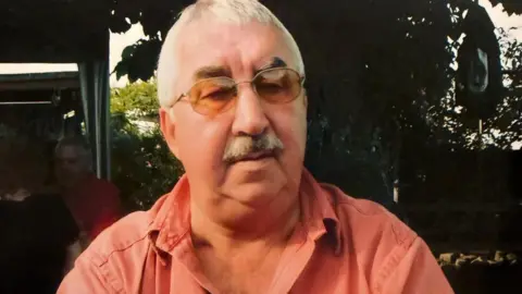 Sean Hayes James Hayes in an archive image. He is wearing sunglasses and a pink shirt. He has short white hair and a grey moustache.