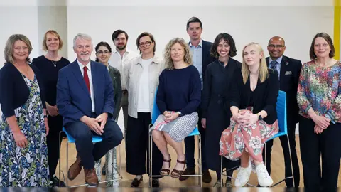 Welsh government 12 people - eight women and four men stood/seated in a semi-circle for a photo-opp.