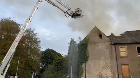 Firefighter sprays water from an aerial platform on to fire in derelict building