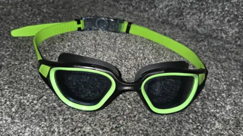 Gina Goldwater A pair of black-lenses goggles with green frames and strap.