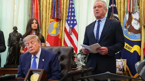 Health and Human Services Secretary Robert F. Kennedy Jr. (2nd-R), accompanied by (L-R) National Institutes of Health Director Jay Bhattacharya, U.S. President Donald Trump, Jayme Leagh Franklin with the The Conservateur, and Deputy Assistant to the President for Domestic Policy Dr. Heidi Overton (R), speaks before Trump signs an executive order calling for childhood vaccine shots to be spaced out into separate visits during an event in the Oval Office of the White House on August 10, 2026 in Washington, DC. 