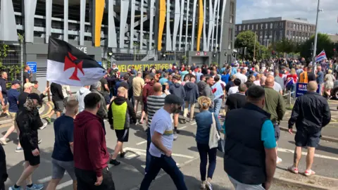 A large group, some with flags, walk away from the camera