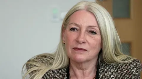 Qays Najim/BBC Kay Mason Billig is looking at the camera. She's wearing a patterned suit jacket.