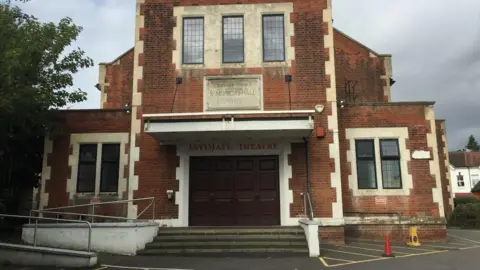 Theatres Trust The red-brick exterior of the Intimate Theatre in north London, with the entrance beneath a sign reading "Intimate Theatre" and a stone plaque marked "St Monica's Hall 1931".