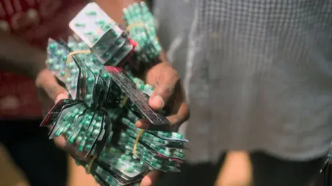 Hands carrying more than 30 bodies of green and white capsules.