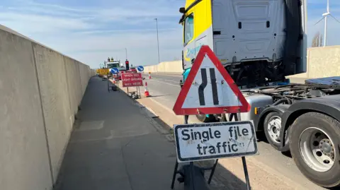 John Devine/BBC Traffic signs and vehicles on a section of a bridge. There is s sign for single file traffic controlled by traffic lights.