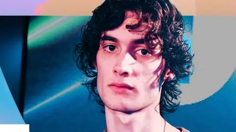 Sombr has wavy brown hair and looks pensive