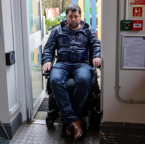 Access Cornwall A man tries to navigate his wheelchair through a narrow doorway. 