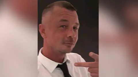 Norfolk Police A selfie of Joshua McAloon who is looking directly at the camera. He has short brown hair and is wearing a white shirt and black tie.