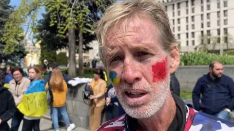 AFPTV/AFP via Getty Images This screengrab taken from AFPTV shows Ryan Wesley Routh at a protest supporting Ukraine in April 2022. Routh is wearing an American flag shirt and has face paint in the colours of the Ukrainian flag on his cheek.