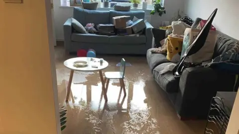 Water covering the living room floor and items on the sofa for safe storage