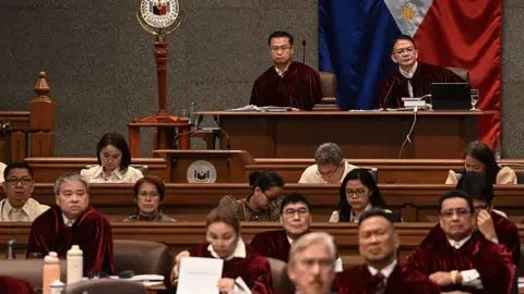 Getty Images Senator-judges in the impeachment trial of Philippine Vice-President Sara Duterte sit in the plenary hall wearing deep red robes