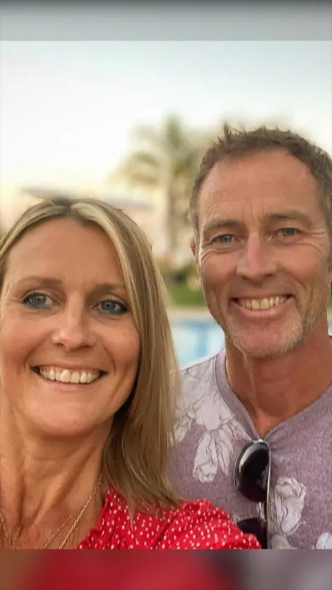A selfie of a man and a woman. She is wearing a red polka dot dress and he is wearing a violet shirt.