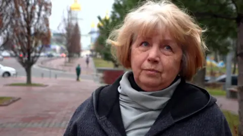 A Ukrainian older woman with blonde hair, a grey coat and grey scarf