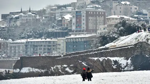 AFP Two people take photos from a white-covered beach with the seaside resort town behind them