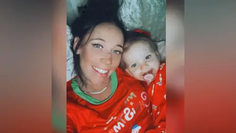 Kerry Blackaller, a woman with black hair, lies down with her daughter. They have matching red tops on.