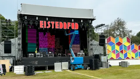 A cherry picker-style machine by the National Eisteddfod stage as final preparations are made for the festival, with eisteddfod written in large letters above the stage