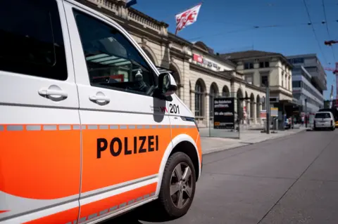 Mid-shot of a white and orange Swiss police van parked outside the Winterthur train station.