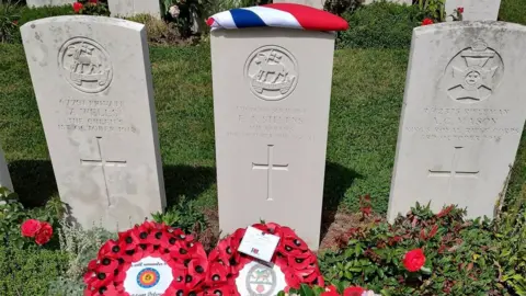 Three Commonwealth war grave headstones in a cemetery, engraved with names, ranks and October 1918 dates, with red poppy wreaths placed at their base.