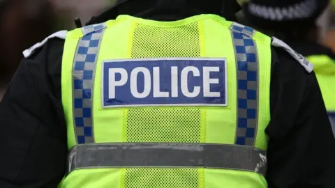 A generic image of a police officer wearing a yellow hi viz vest with the word "Police" visible 