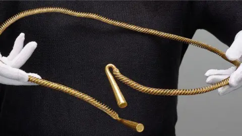 Trustees of the British Museum Bronze Age torc found in Cambridgeshire being held by a person wearing white gloves