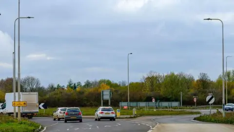 LDRS Image of the A16 round about with cars driving around it and street lamps can be seen on either side of the road.