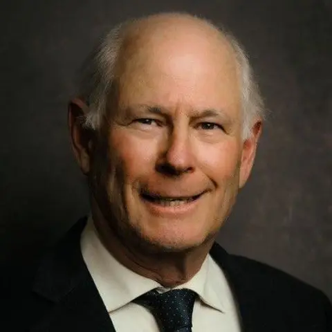 Jonathan Schneer A man with short grey hair smiles for the camera. He is wearing a navy tie with small white spots, white shirt and black jacket. 