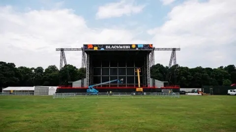 Rhodes Media The Blackweir Live concert stage seen on a field with fencing around it. There are tents and construction equipment on either side.