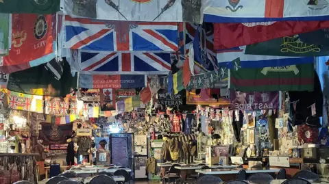 Julie Cooper The inside of The Last Post which has flags covering the ceiling and memorabilia can be seen on the wall in the background. 