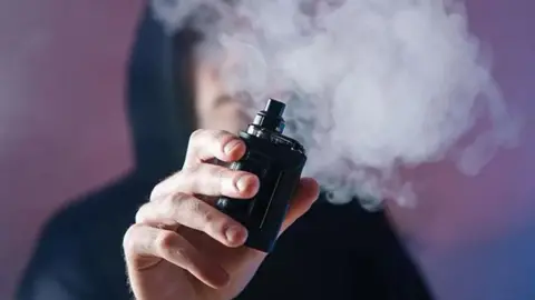 A person in a hoodie smoking a vape 