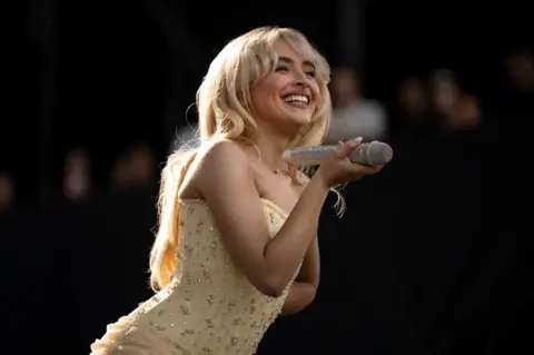 Reuters Sabrina Carpenter smiles while holding a microphone on stage