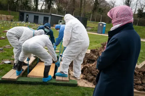 PA Media People in hazmat suits burying a coffin