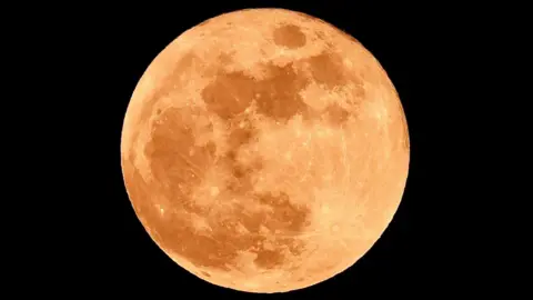 Full moon with a light-ish red tint. You can see the darker spots of the moon. Taken from Woodham in County Durham. The sky surrounding the moon is pitch black. 