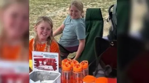 Lydia Jemima and Isabel at a table selling things at a fundraising event.