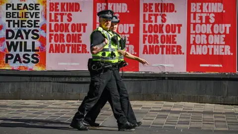 Getty Images Two police officers walk past posters in Glasgow, Scotland