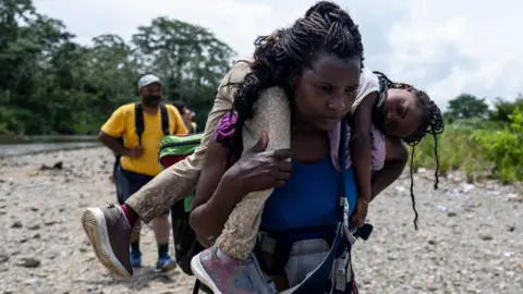 Una mujer migrante camina por el bosque cargando a su hija cerca del pueblo de Bajo Chiquito, el primer puesto de control fronterizo de la provincia de Darién en Panamá, el 22 de septiembre de 2023. 