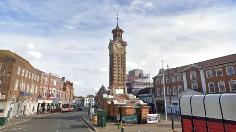 A brick clock tower in the middle of an English town.